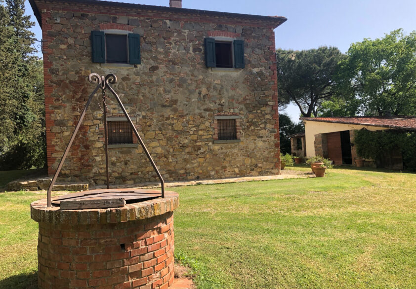 Traditional stone farmhouse with well in Tuscany countryside.
